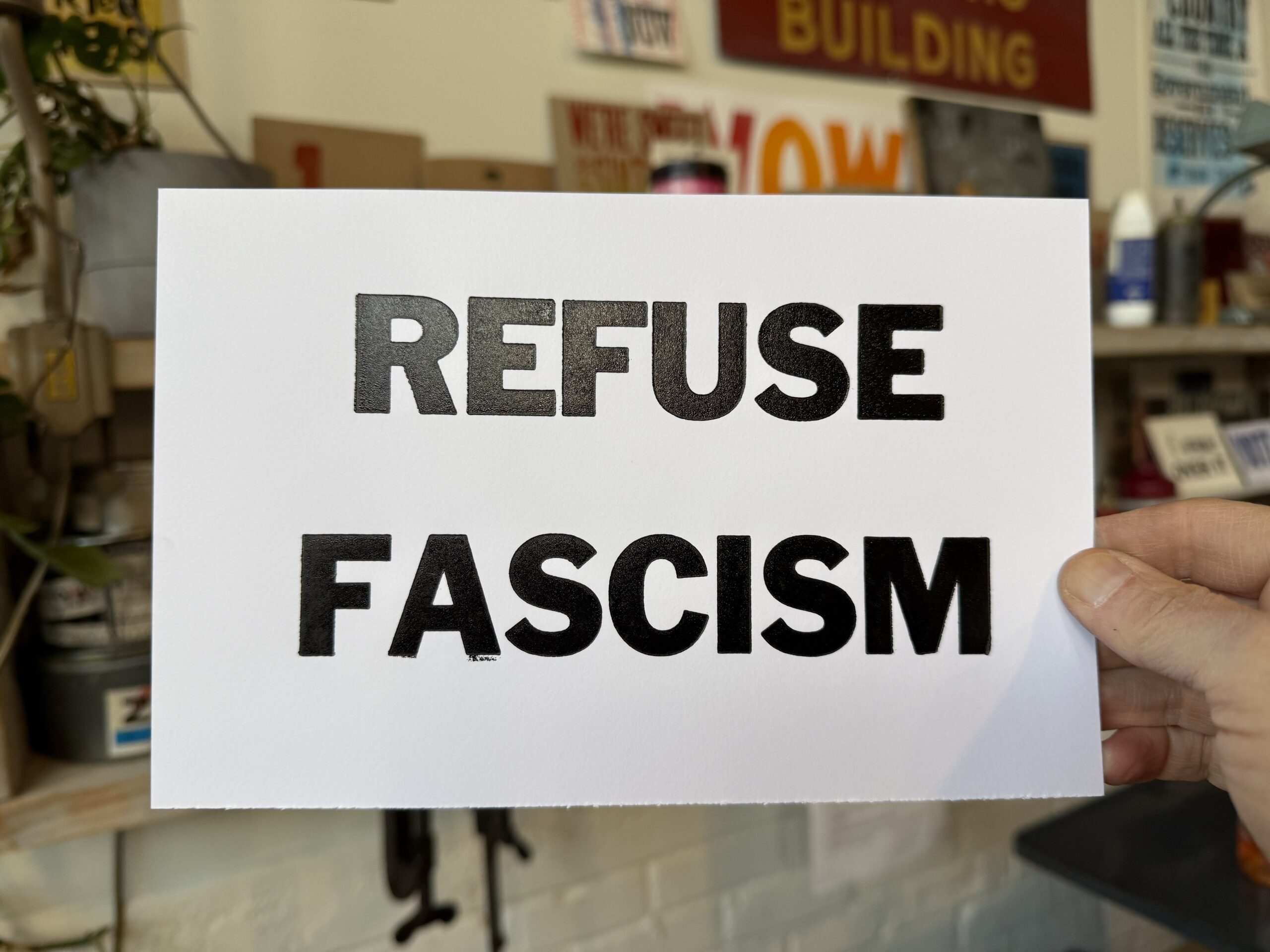 A hand holding a sign that says, "REFUSE FASCISM"